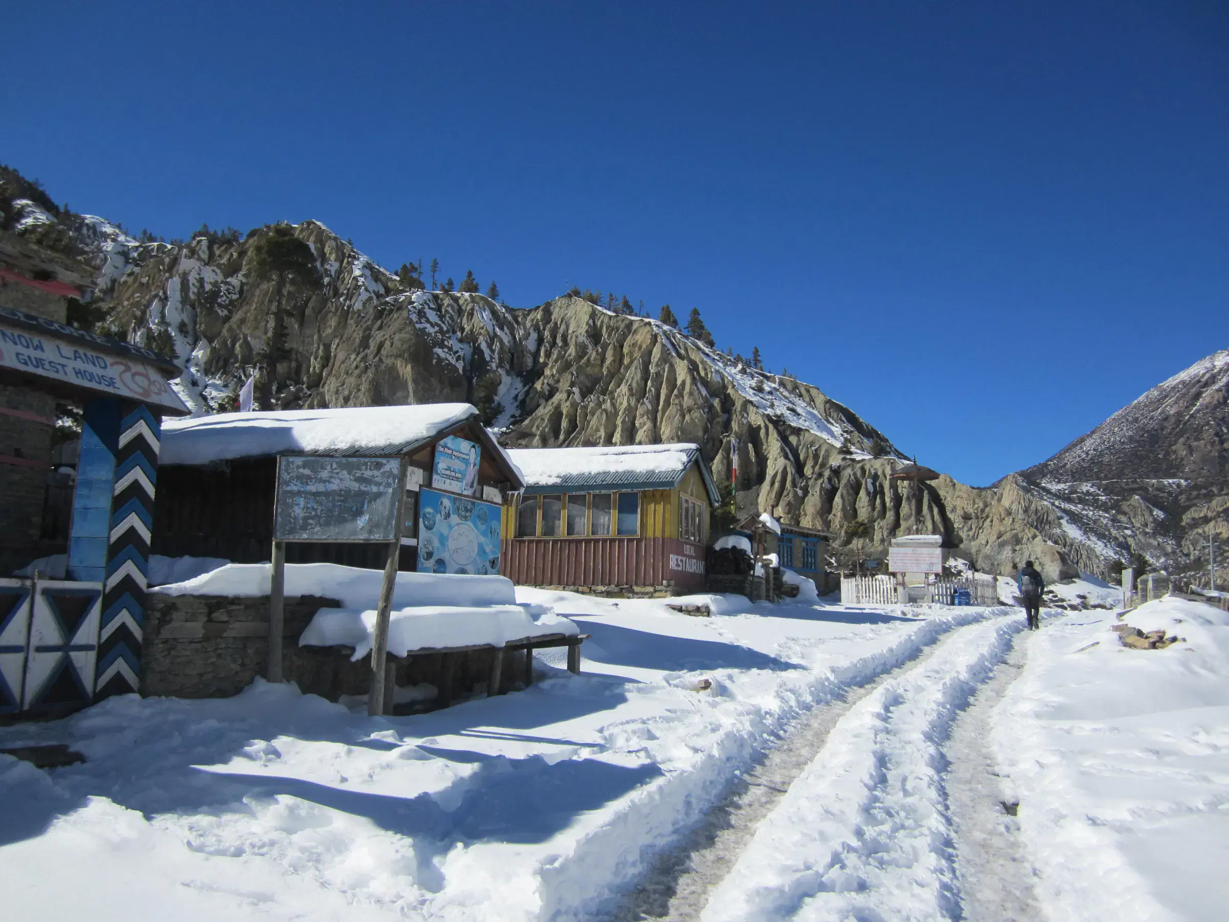 Mountain landscape featuring snowy terrain, water, a built structure, and blue sky.