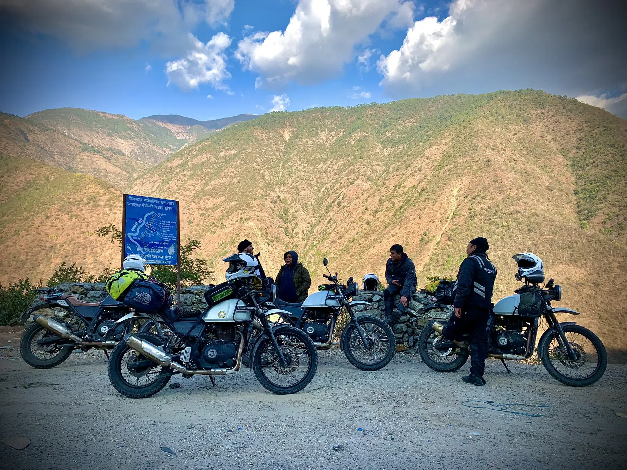 Outdoor adventure scene featuring people, a vehicle, rocky terrain, and cloudy sky.