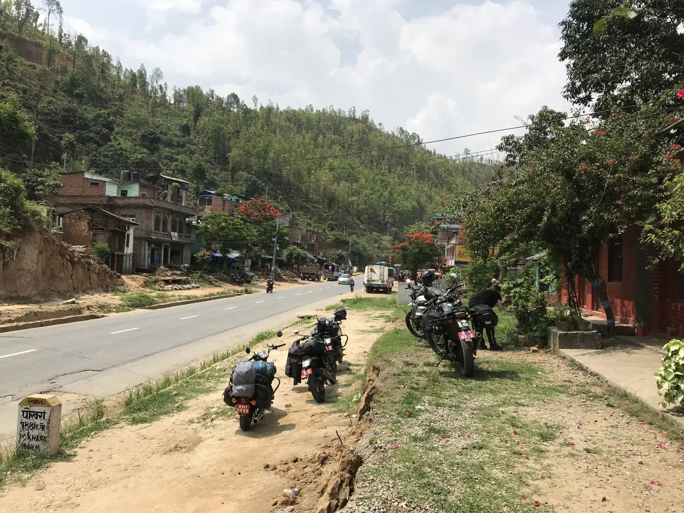 Outdoor vehicle scene featuring a vehicle, rocky terrain, cloudy sky, and greenery.