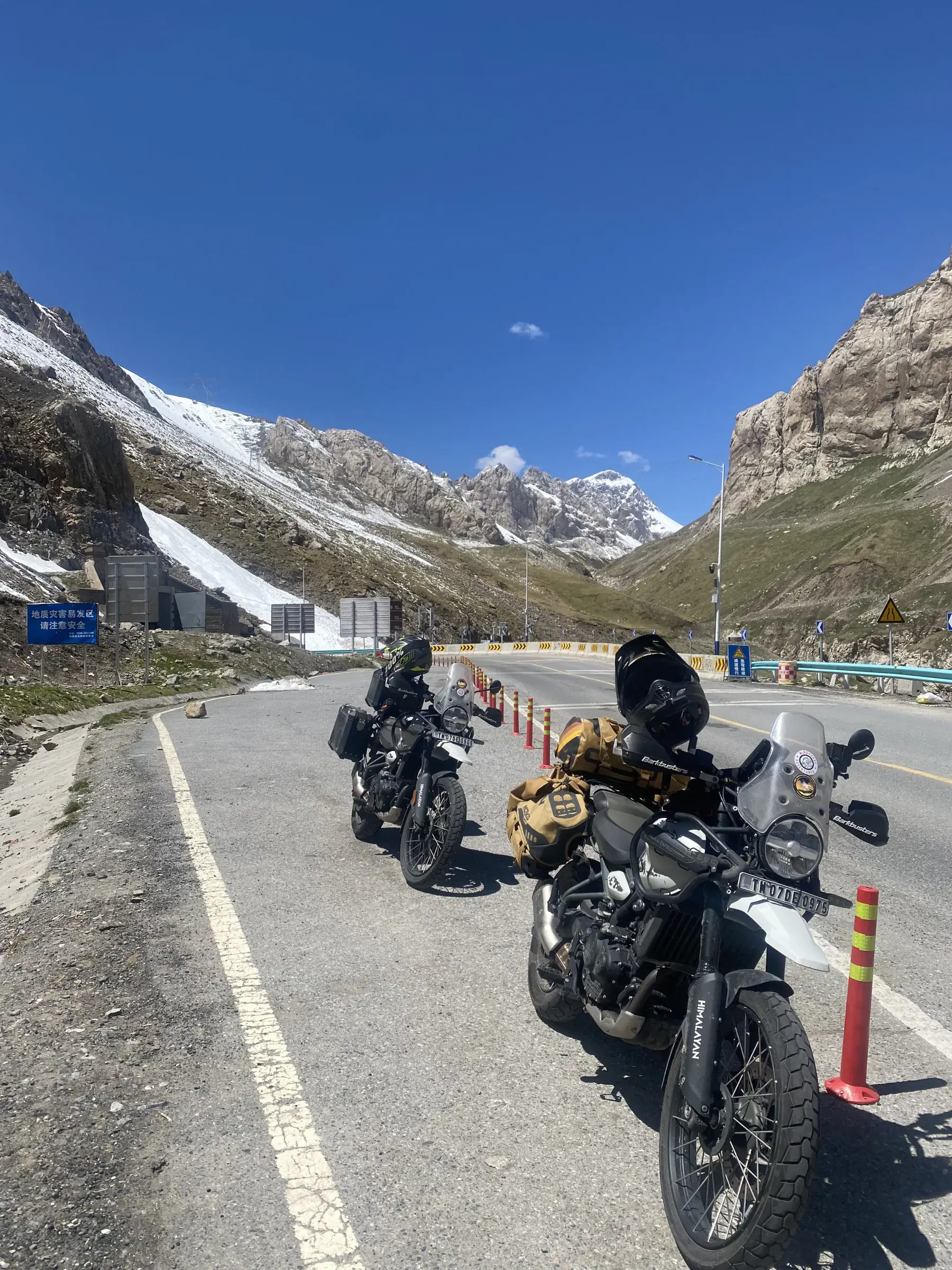 Outdoor vehicle scene featuring a vehicle, rocky terrain, a built structure, blue sky, and greenery.