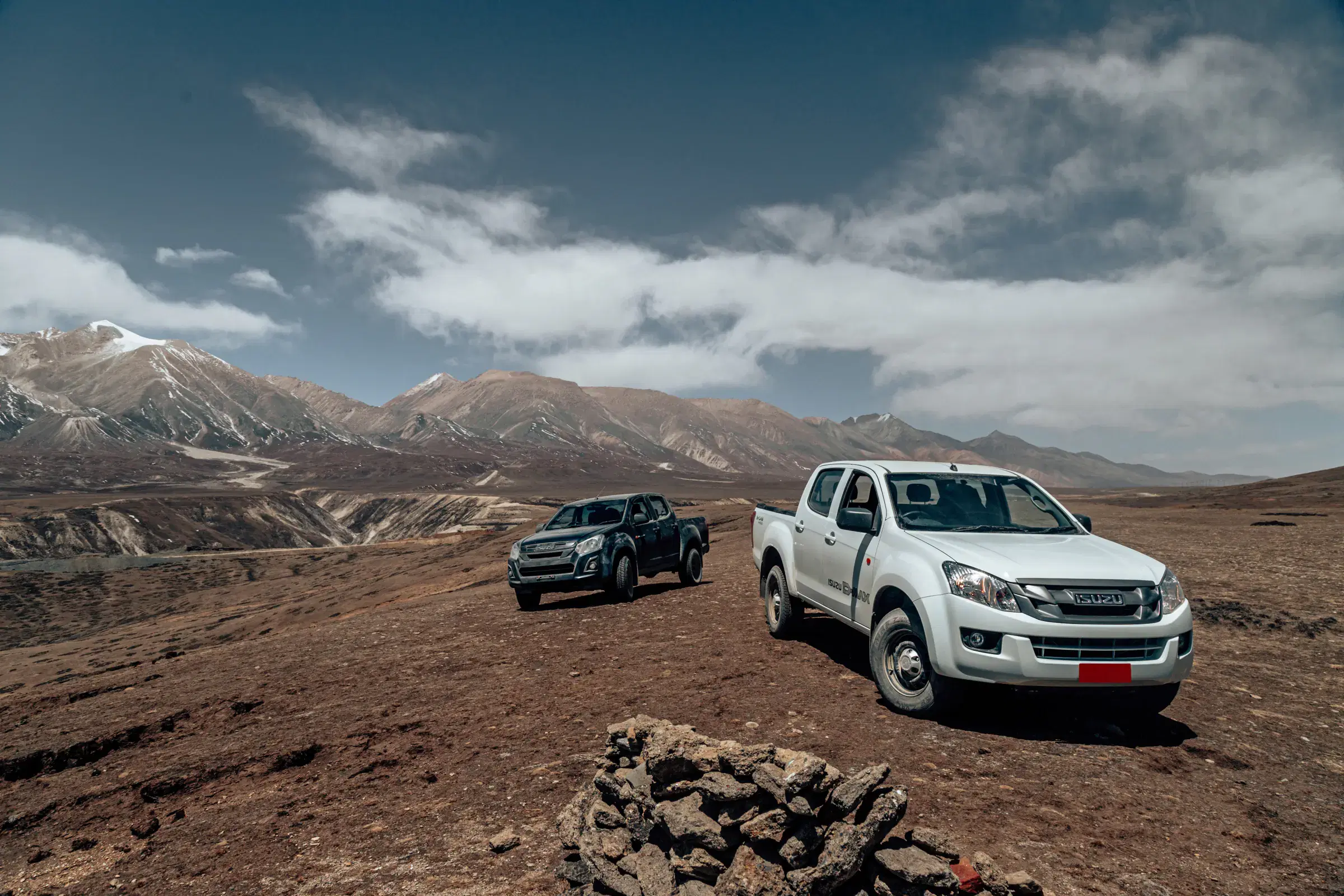 Outdoor vehicle scene featuring a vehicle, rocky terrain, a built structure, and cloudy sky.